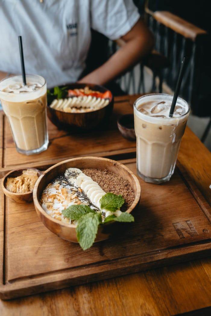 home-hero-2 Delicious breakfast bowl with banana and iced coffee on a wooden table.