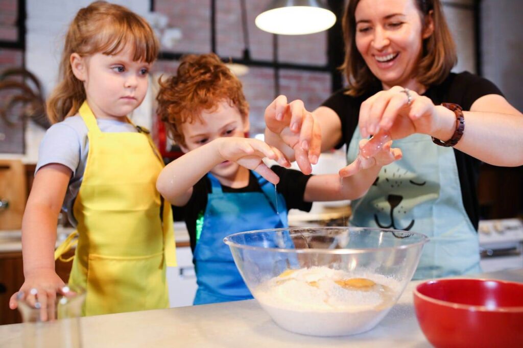 Children and a woman joyfully baking cookies together, learning cooking skills.