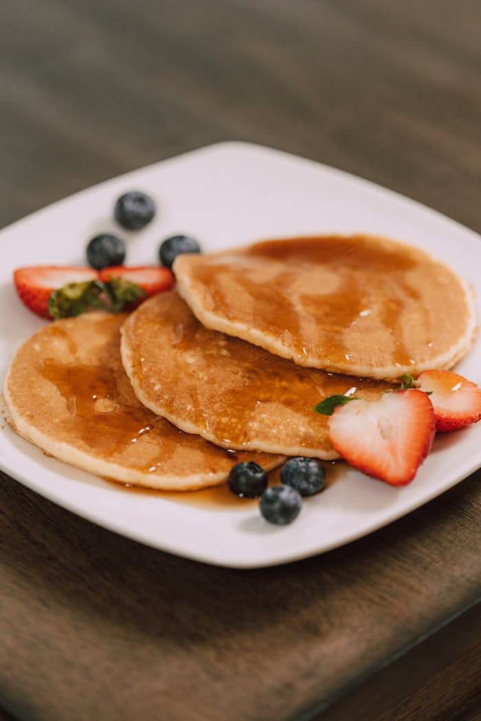 services-03 Mouth-watering pancakes served with fresh strawberries, blueberries, and syrup on a white plate.
